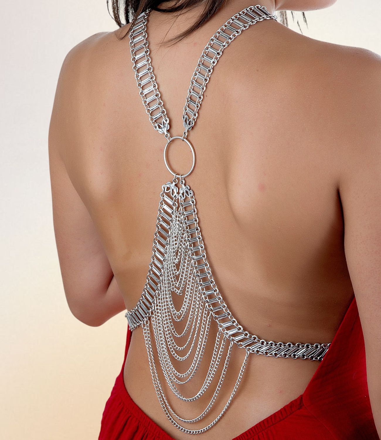 A silver spine jewelry piece draped across a woman's bare back, featuring multiple layered chains hanging from a central ring, styled with a red backless dress.