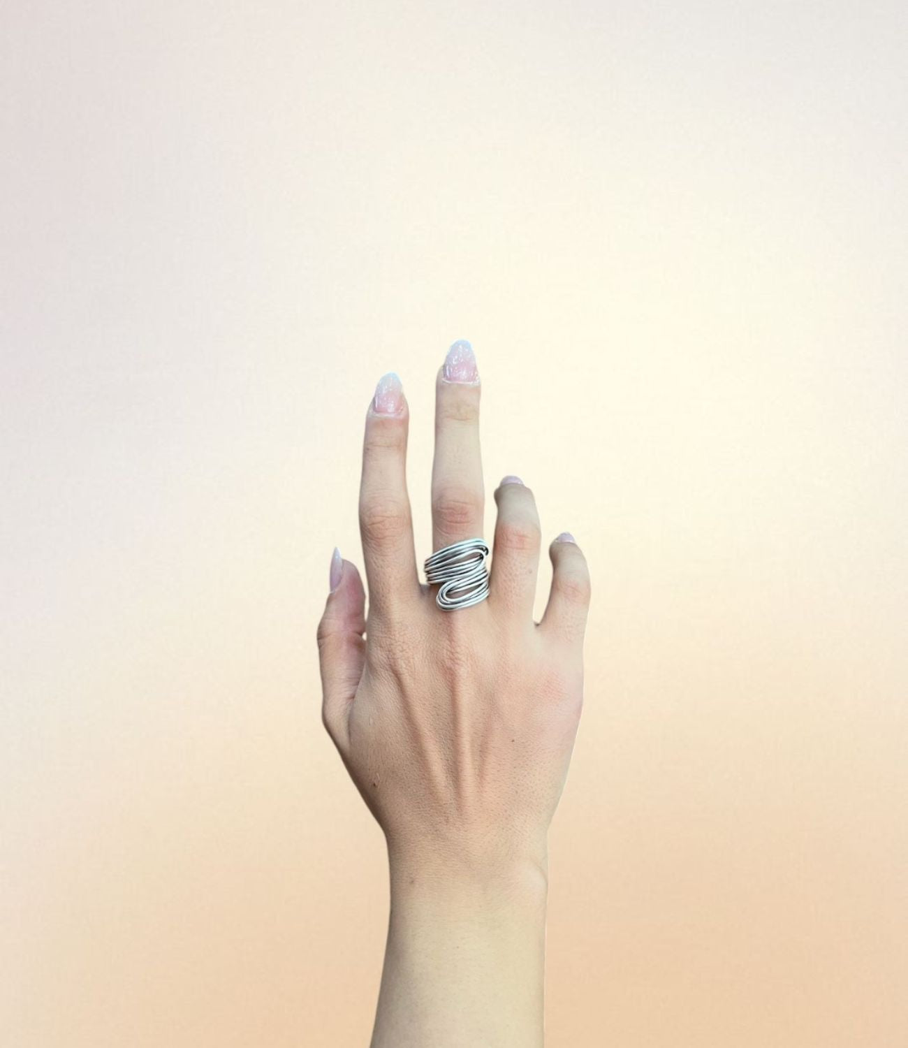 A hand wearing the Flow Ring — a silver-plated ring made of layered, wire-like bands that curve around the finger in a flowing, sculptural design.
