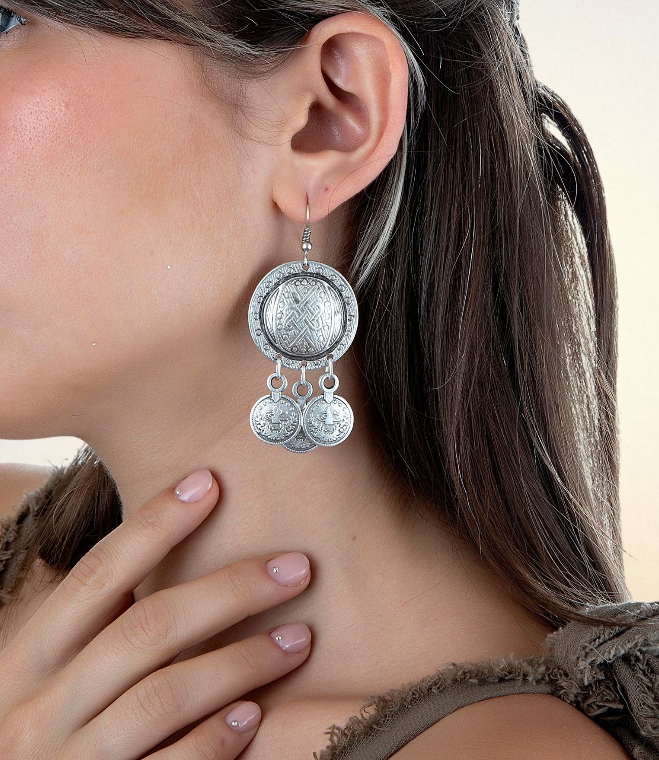 Close-up of a woman's ear wearing the Jingle Coin Earring — a large silver medallion with intricate engravings and three dangling Ottoman-style coin charms, creating a bold and traditional statement.