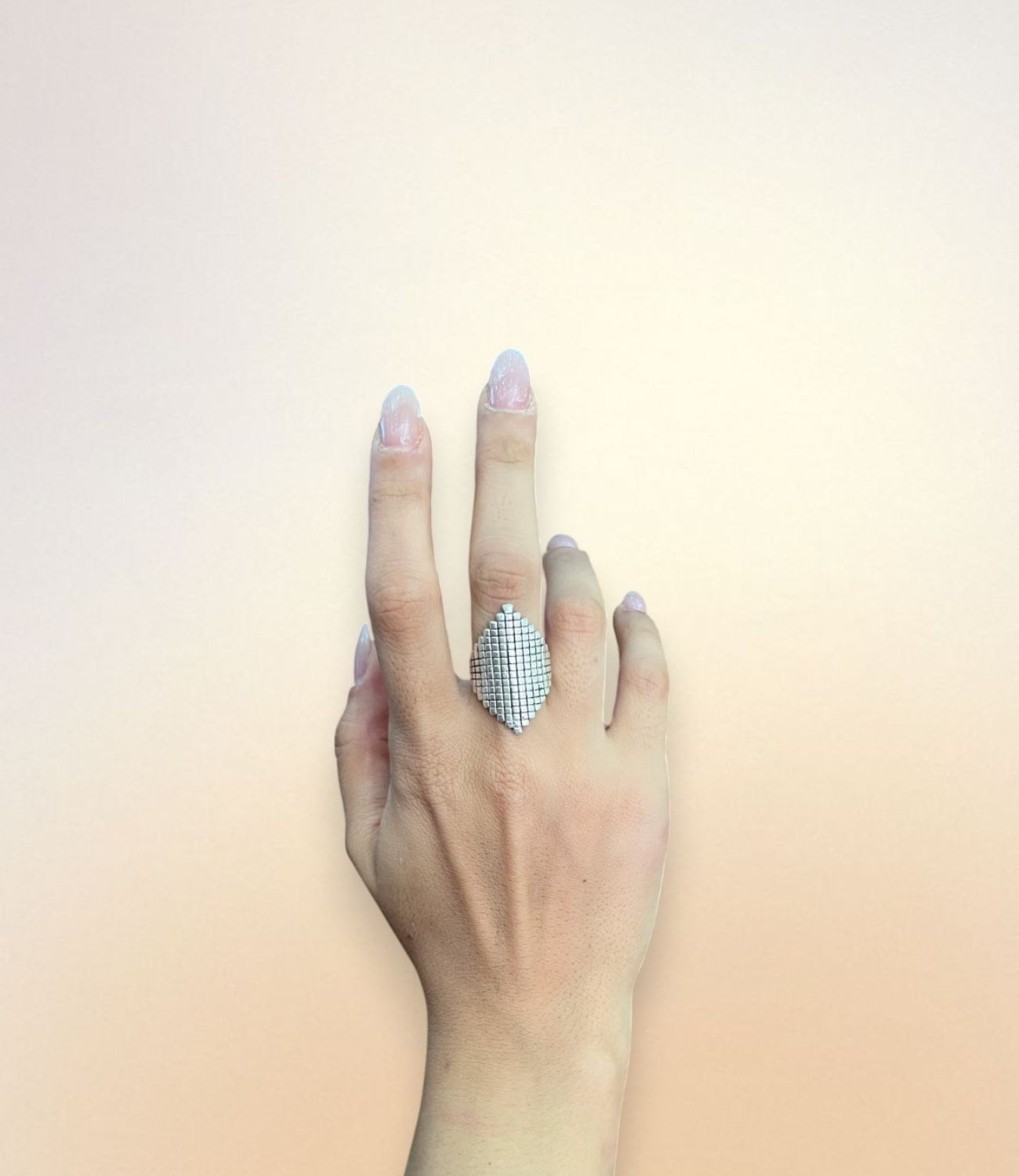 A hand wearing the Pixel Ring — a silver-plated ring with a diamond-shaped top and grid texture, combining clean geometry with bold minimalism.