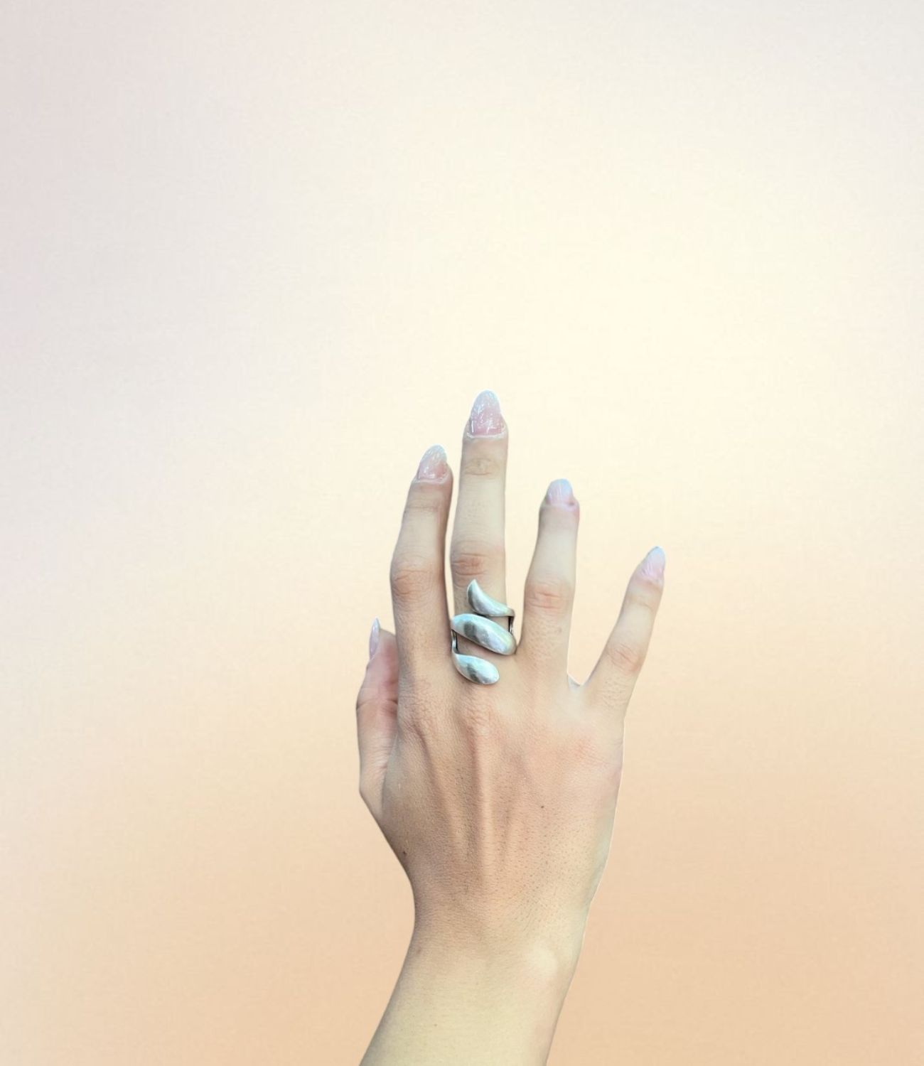 A hand wearing the Ripple Ring — a silver-plated ring featuring three curved, wave-like bands that wrap gently around the finger in a fluid, organic shape.