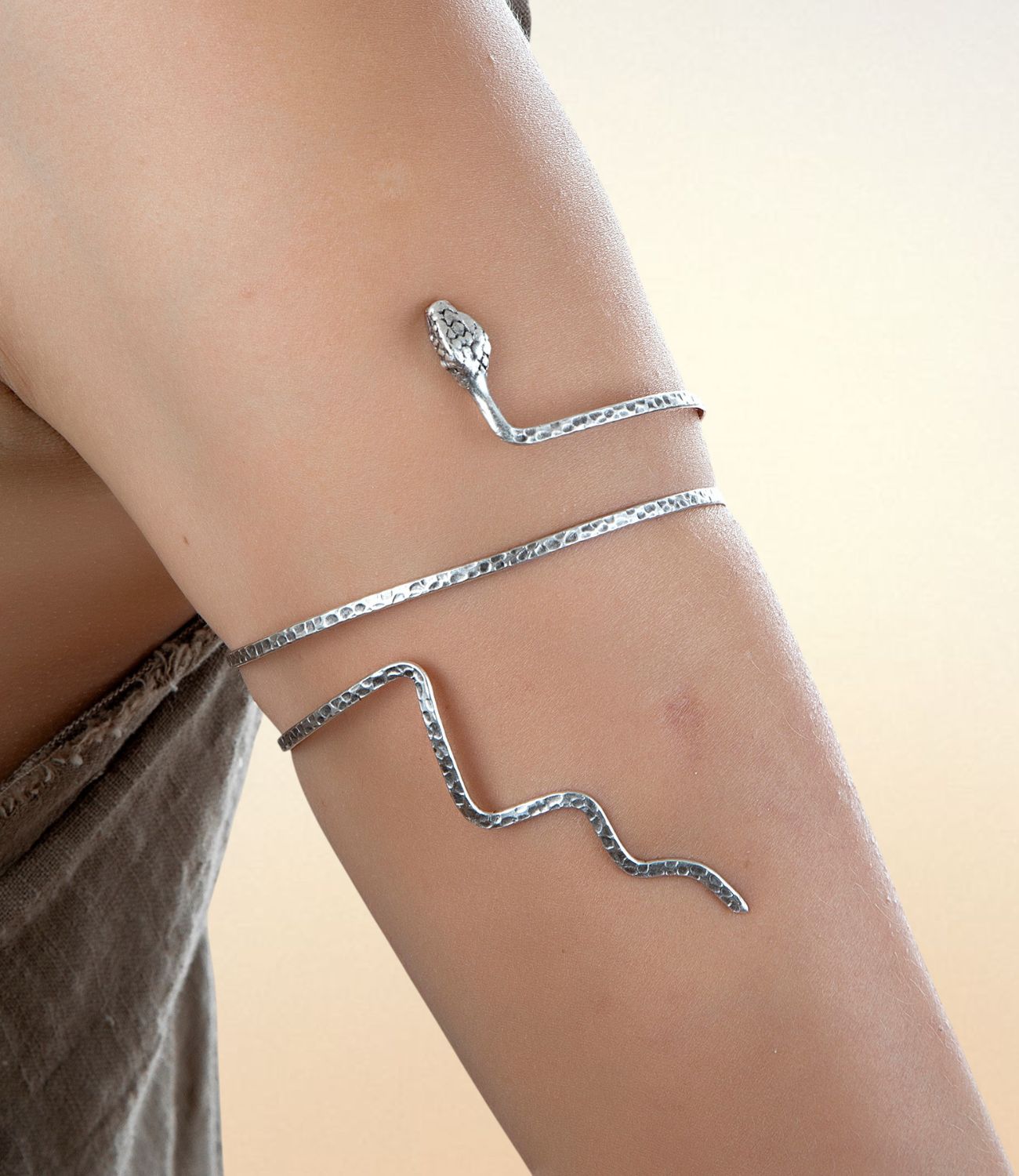 Hammered silver snake-shaped arm cuff wrapped around the upper arm, featuring a detailed snake head and coiled body.