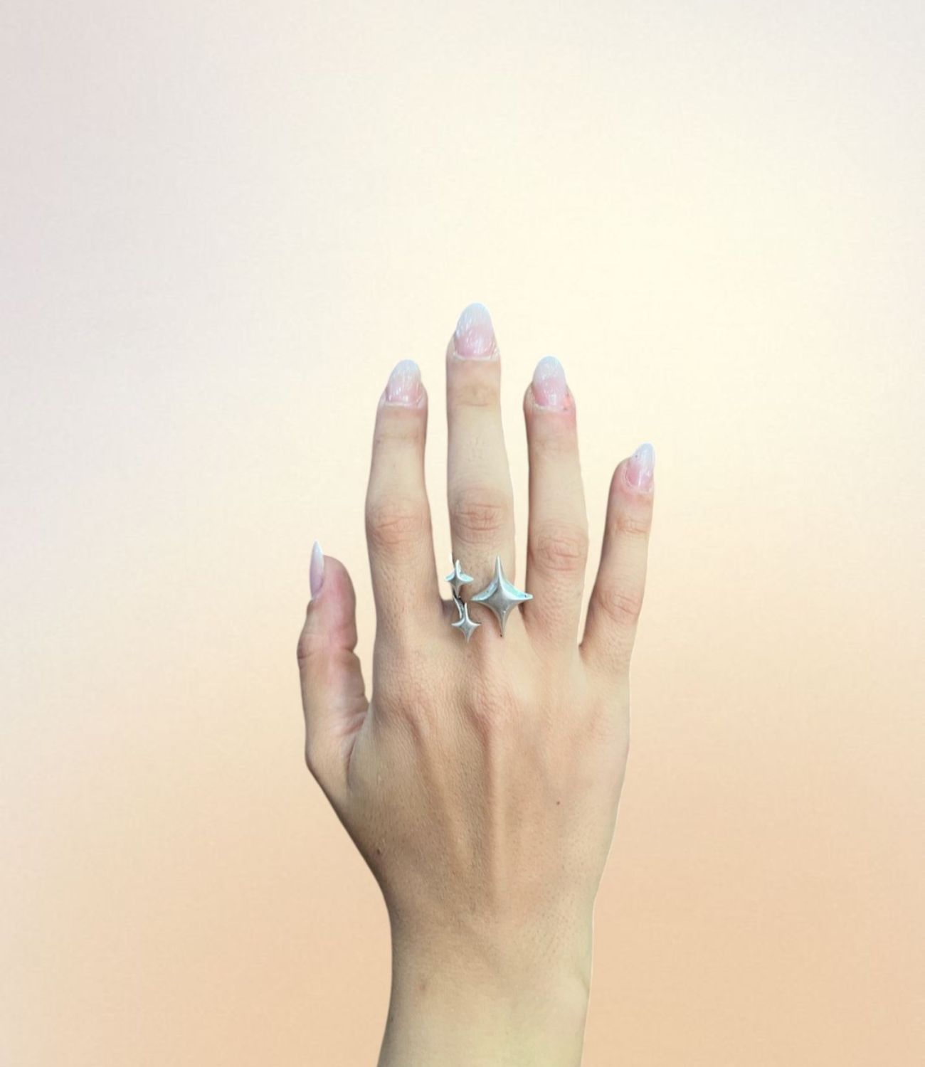 A hand wearing the Sparkle Ring, designed with three silver abstract star shapes arranged along an open band, giving the look of twinkling stars across the finger.