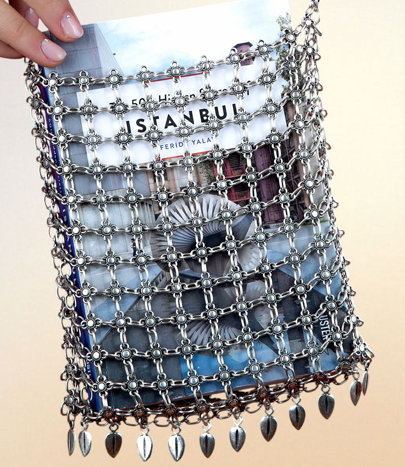 Metal chain bag with floral-linked design and dangling leaf charms, holding an Istanbul-themed book.