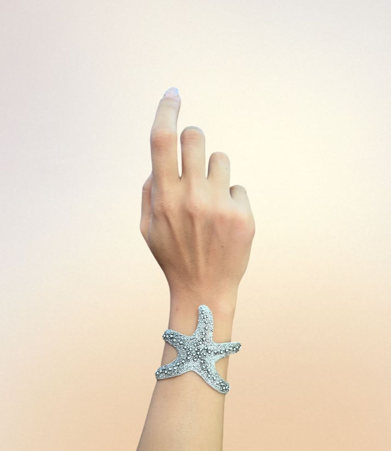 Silver starfish-shaped cuff bracelet worn on wrist, featuring a textured, ocean-inspired design.