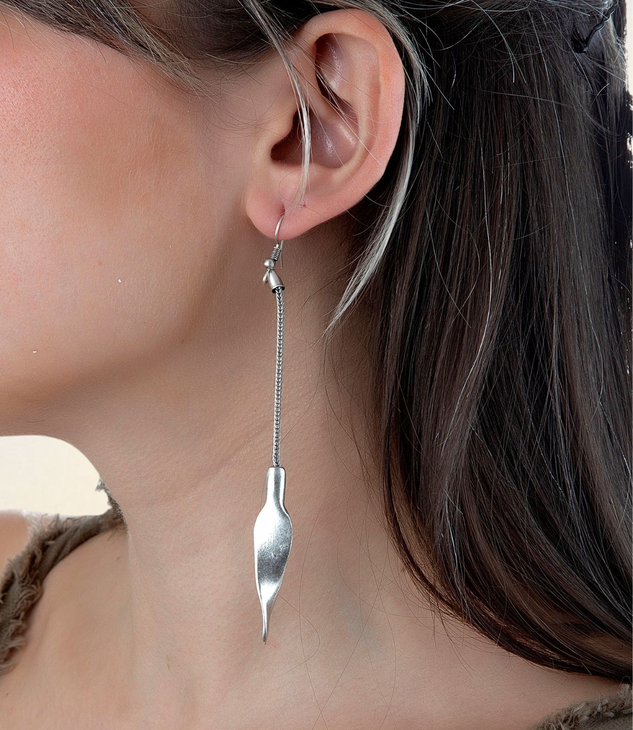 Close-up of a woman wearing the Teardrop Earring — a long, silver earring featuring a delicate chain and abstract teardrop-shaped end, creating a modern, minimal silhouette with graceful movement.