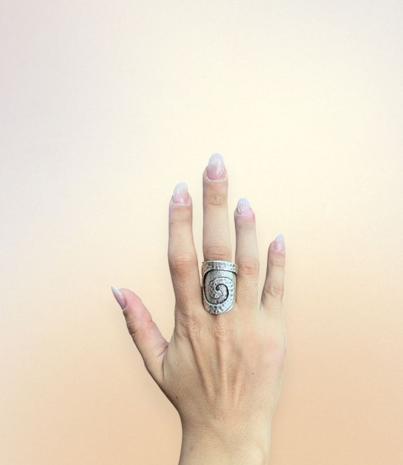 A hand wearing the Whirl Ring — a bold silver-plated ring with a wide hammered band and a swirling carved design in the center, evoking natural movement and timeless symbolism.