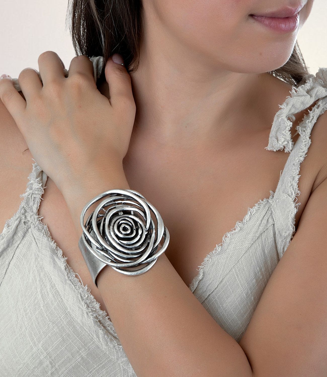 A bold silver cuff bracelet featuring a large, abstract flower design made of layered loops, worn on a crossed arm over a textured cream top.