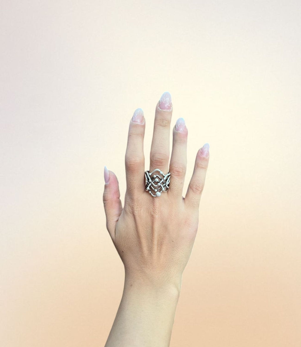 Hand wearing the Galaxy Ring – silver ring with layered criss-cross design and small sphere accents inspired by planetary orbits