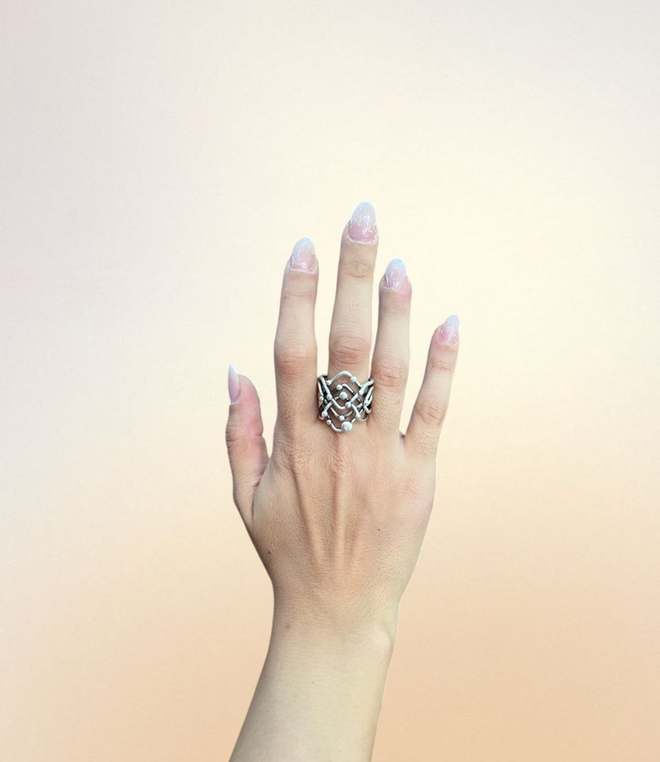 Hand wearing the Galaxy Ring – silver ring with layered criss-cross design and small sphere accents inspired by planetary orbits