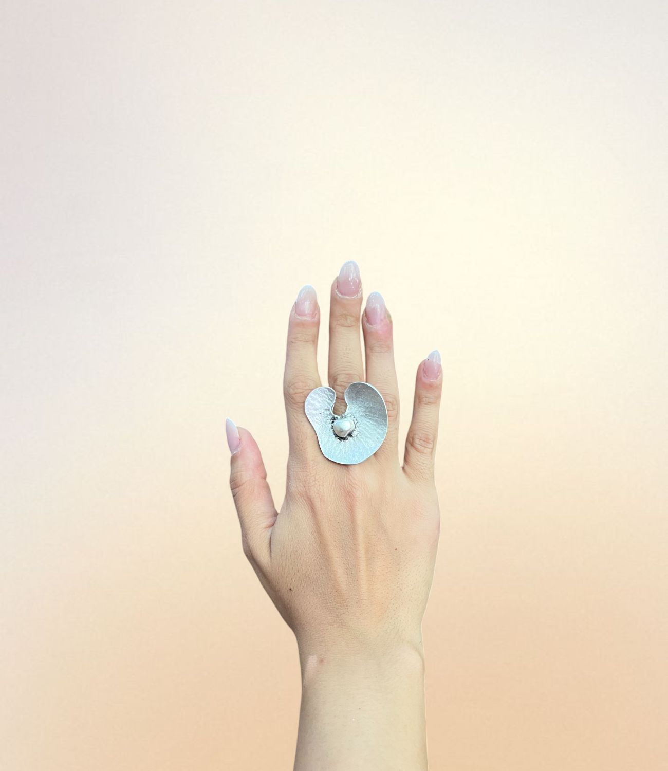 Silver sculptural ring shaped like an abstract orchid with a round white bead at the center, worn on hand
